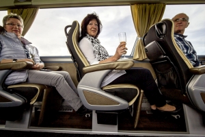 Passagiere sitzen entspannt mit viel Beinfreiheit im First Class Bus und trinken Sekt