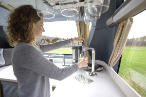 Crewmitglied schenkt in der Bordküche ein Bier im First Class Bus ein
