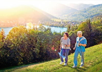 Mann und Frau gehen mit Walking Stöcken spazieren und blicken auf Berge und einen See