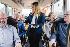 Servicekraft im First-Class-Bus verteilt einen Begrüßungssekt an die Fahrgäste