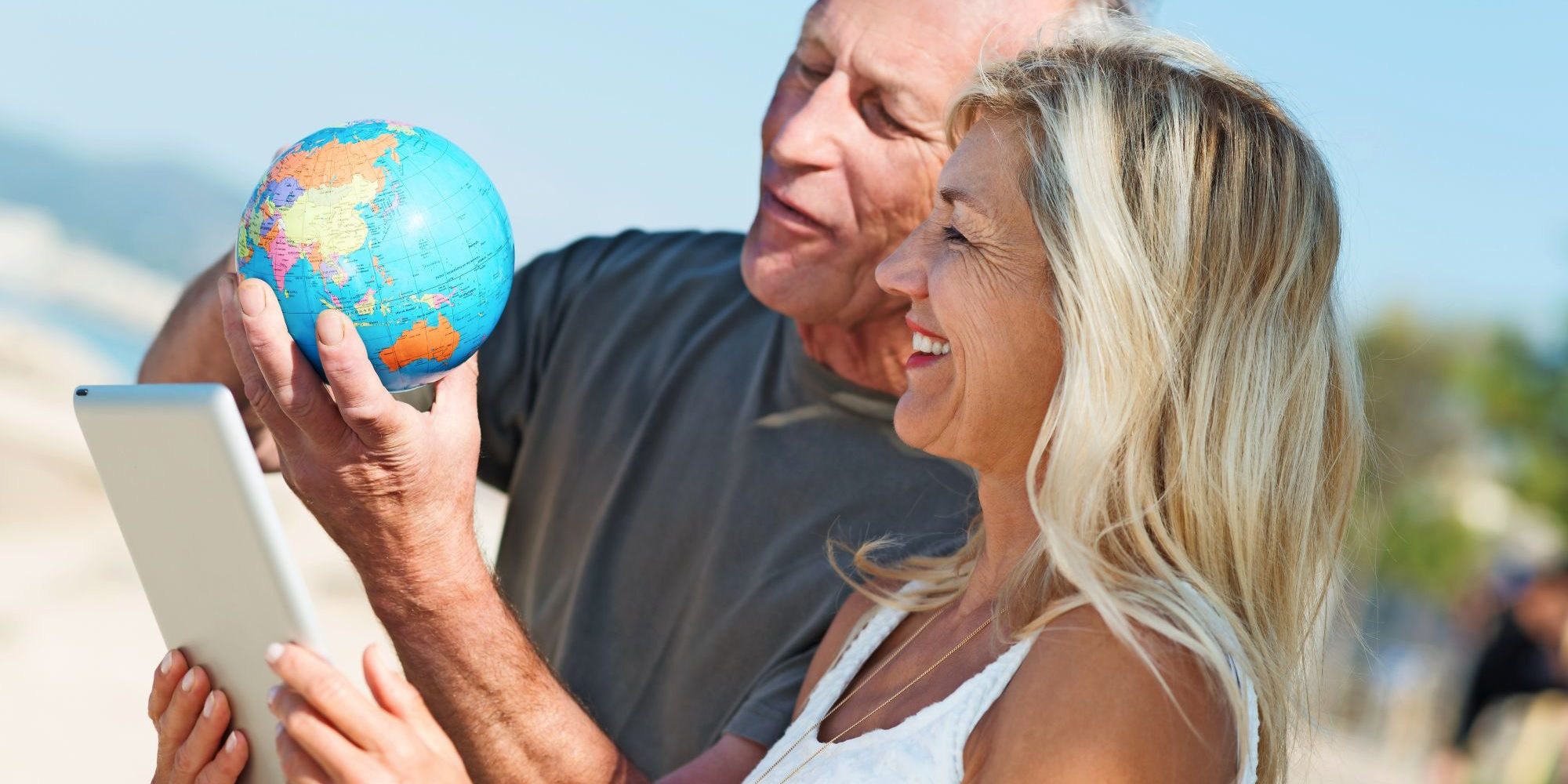 Mann hält eine kleine Weltkugel und Frau hält ein Tablet beide stehen am Strand und schauen auf die Weltkugel