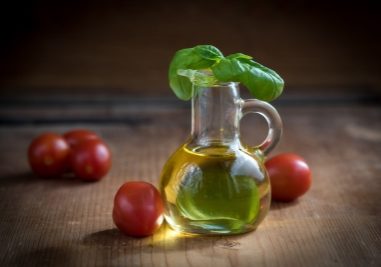 Olivenöl in einer Karaffe mit Basilikum Blatt steht auf einem Holztisch und umringt von Kirschtomaten