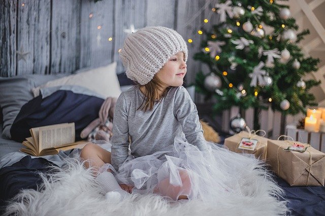 Mädchen mit Weihnachtsgeschenken sitzt auf einer Kunstfelldecke