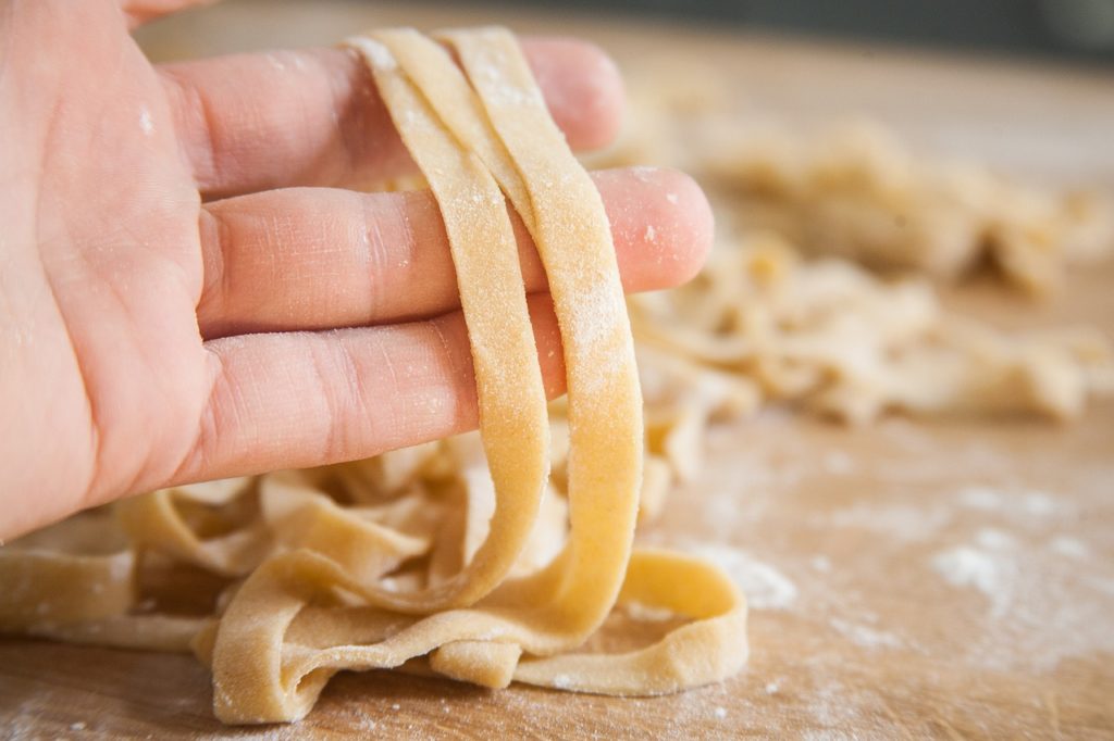 Hand hält frisch geschnittene leicht mehlige Pasta hoch