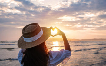 Dame formt Herz aus Fingern bei Sonnenutnergang