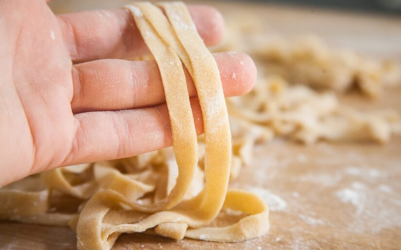 Hand hält frisch geschnittene leicht mehlige Pasta hoch